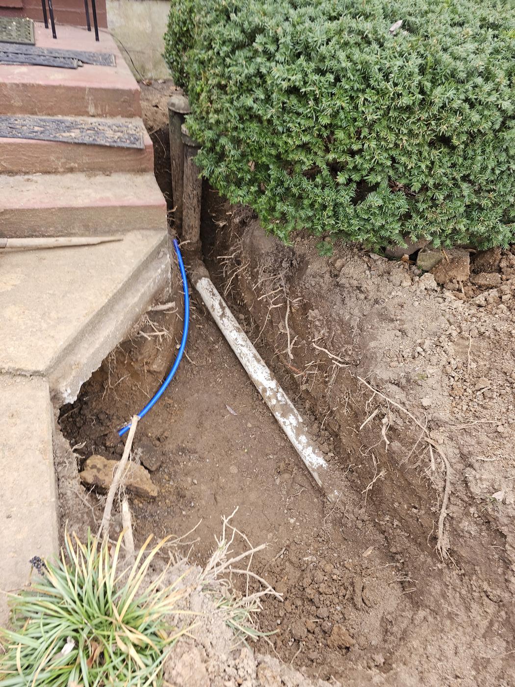 An open trench beside a house with a new water line run along the bottom